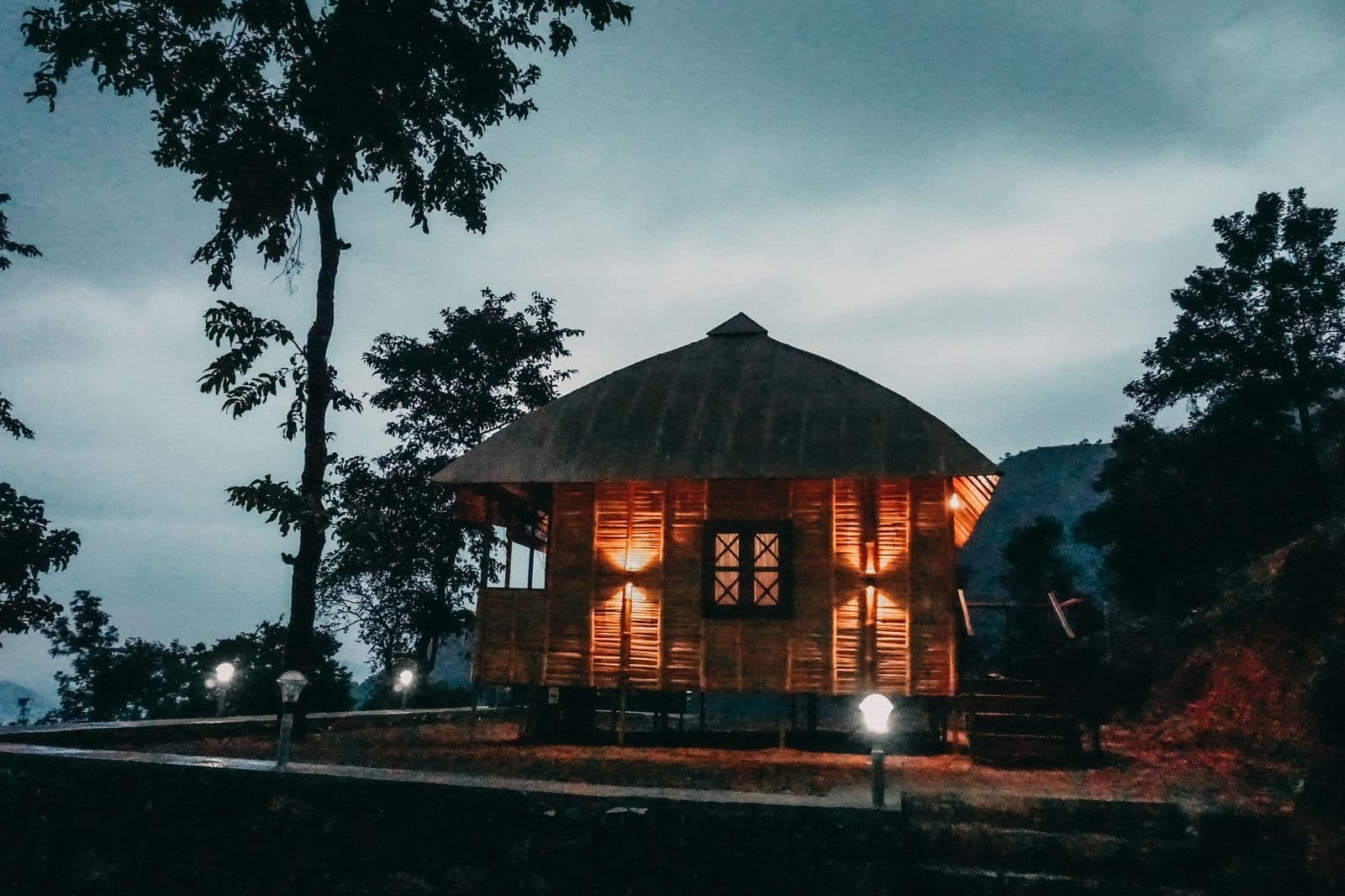 A bamboo cottage at dusk, lamps lit, above the Urumbikkara valley